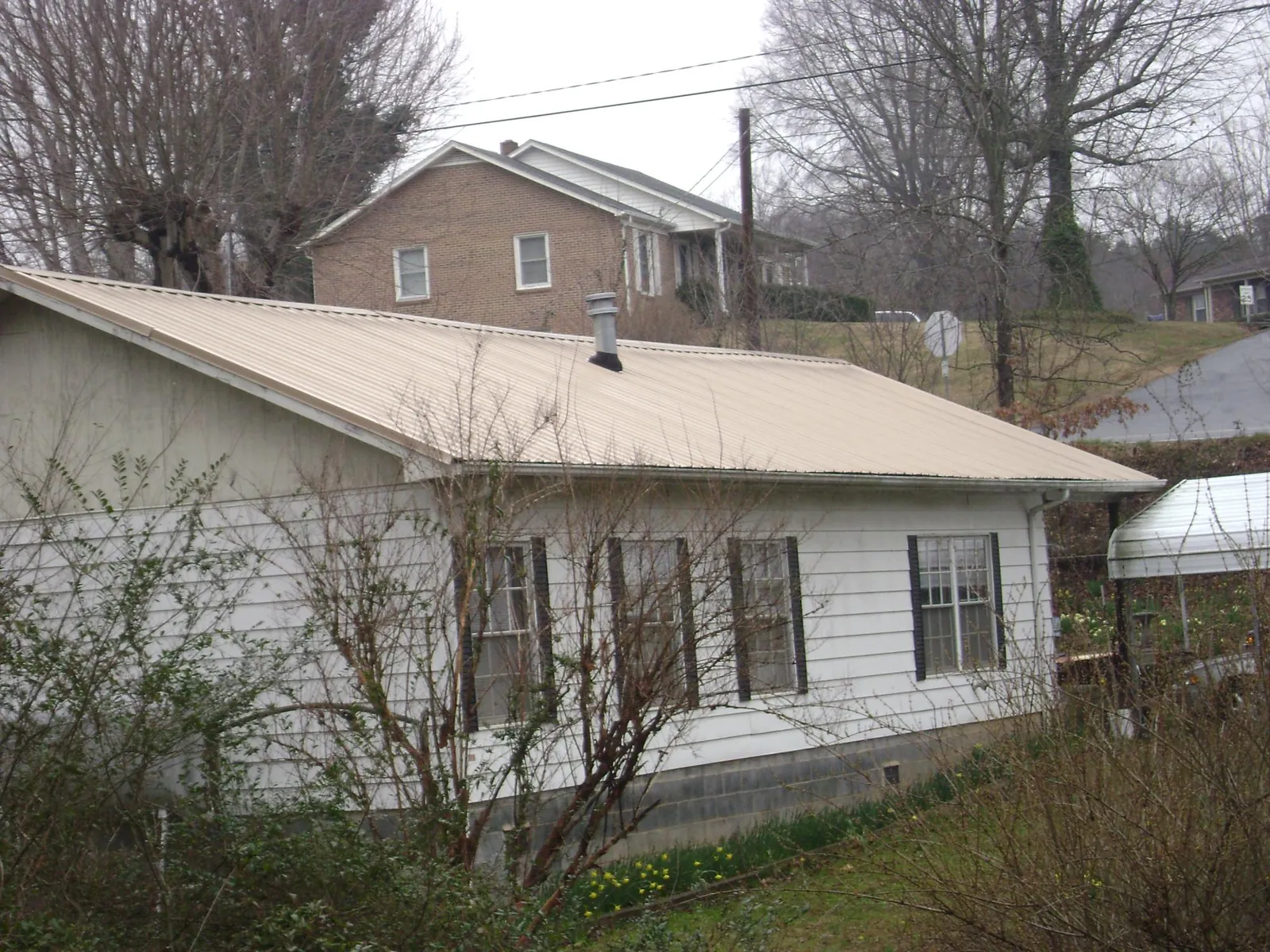 Tan metal roof on a white sided house set into a hillside — Commercial Roofing by Roofing Brothers in Whitehall